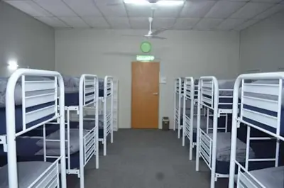 a room with rows of bunk beds and a green clock at Bed Station Guest House in Tanah Rata