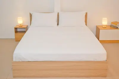 a bed with white sheets and two lamps on tables at Singah in Bukit Mertajam