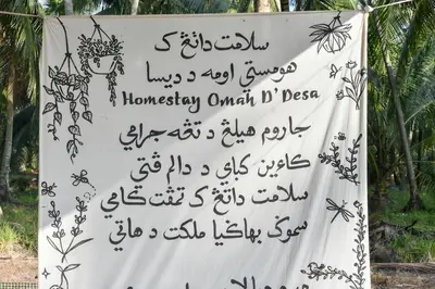 a sign with writing on it next to trees at Homestay Omah D'Desa with pool in Kampong Telok Ru