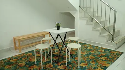a table and four stools on a rug with a staircase at Eyna Homestay in Sitiawan