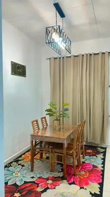 a dining room with a table and chairs on a rug at Madam Cottage Homestay in Sungai Petani