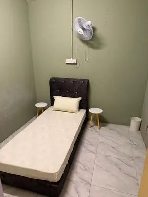 a bed in a room with two tables and a fan at Rina Hostel in Ipoh