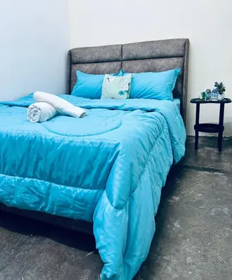 a blue bed with a blue comforter and a table at Little Stay Inn in Taiping