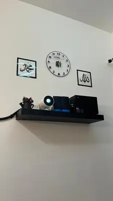 a shelf with a clock and pictures on a wall at Teratak Burung Darimi in Kampong Bota Road