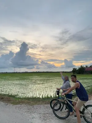 two people riding a bike in front of a field at The Canal Villa in Sungai Besar