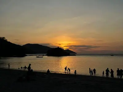 a group of people on the beach at sunset at Azure Haven - Seaview Resort Home, By the Sea Batu Ferringhi in Batu Ferringhi