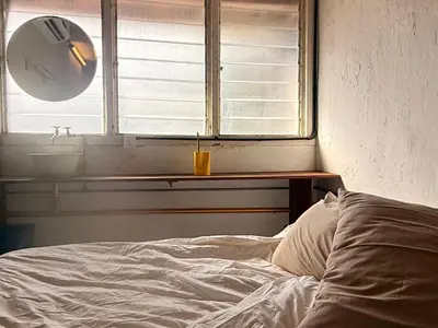 a bedroom with a bed and a window with a sink at Just House - Rooms & Curios in George Town