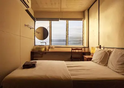 a bedroom with a bed and a window with a chair at Just House - Rooms & Curios in George Town