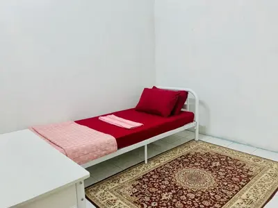 a small bed with a red pillow and a rug at Homestay Hayyan