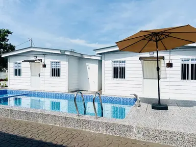 a pool with an umbrella next to a building at Rossaliya Cottage in Taiping