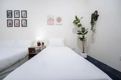 a white bedroom with two beds and a plant at Georgetown Heritage 1F stay 10pax 3BR in George Town