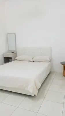 a white bedroom with a white bed and a table at Rara Homestay in Kampong Selamat