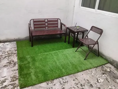 a bench and a table and a chair on a green rug at Room Stay YNS Kampar Putra 1 Bilik dan Bilik Air in Kampar