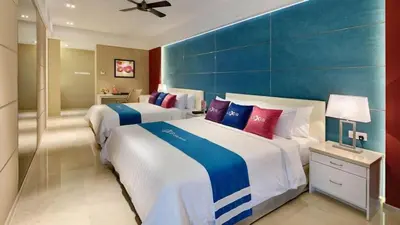 two beds in a hotel room with blue and red pillows at Lexis Suites Penang in Bayan Lepas
