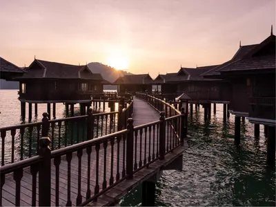 a dock with houses on the water at sunset at Pangkor Laut Resort - Small Luxury Hotels of the World in Pangkor