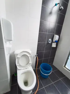 a bathroom with a toilet and a blue bucket at Cameron's Square Apartment in Cameron Highlands
