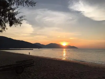a sunset on the beach with a bench on the beach at By The Sea at Batu Ferringhi Penang in Batu Ferringhi