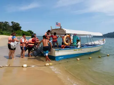 a group of people getting off a boat on the beach at Pangkor Holiday Home in Pangkor