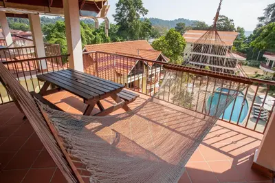a hammock on a balcony with a table and a pool at Anjungan Beach Resort in Pangkor