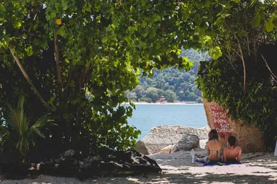 two women sitting on the beach near the water at Anjungan Beach Resort in Pangkor