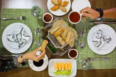 a table with plates of food and a person holding a knife at Sayong Resort in Kuala Kangsar
