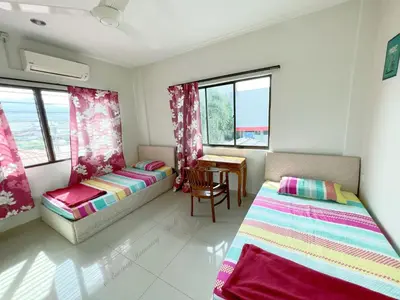 a bedroom with two beds and a table and windows at Buntong Homestay -Rooms Only in Ipoh