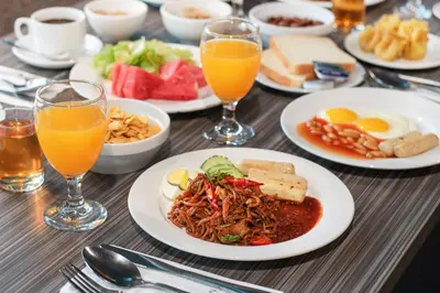 a table with plates of food and glasses of orange juice at Flemington Hotel in Taiping