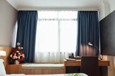 a bedroom with a window with blue curtains and a desk at Hotel Sfera in Lumut