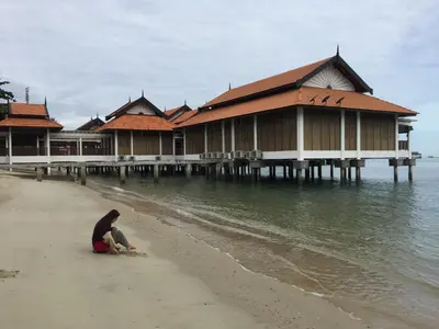 a person sitting on the beach in front of a building at Pangkor Damai in Pangkor