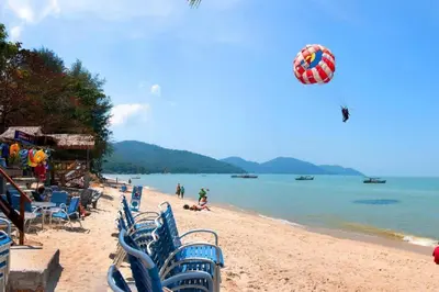 a beach with chairs and a kite flying over the water at 5-BEDROOM FERRINGHI HOUSE with WIFI , NETFLIX , BBQ SET , 5 MINUTES WALK to BEACH in Batu Ferringhi