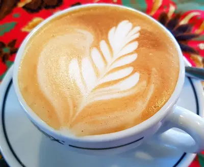 a cup of coffee with a leaf painted on it at Coffee Atelier in George Town