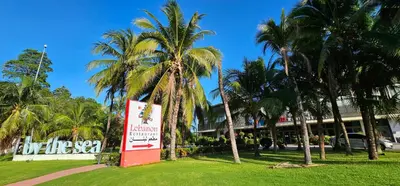 a sign in front of a building with palm trees at By The Sea Beach Luxury Resort - Batu Ferringhi in Batu Ferringhi