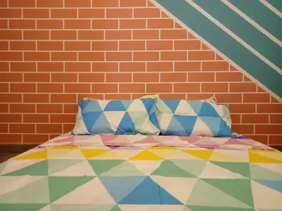 a bed against a brick wall with a colorful comforter at ICOLOR HOME & STAY CH5 in Tanah Rata