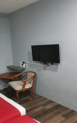a tv on a wall with a chair and a table at Lucky Hotel in Sungai Petani
