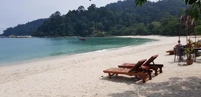 a beach with benches and a boat in the water at Teratak Nipah Homestay Teluk Nipah Pangkor in Pangkor