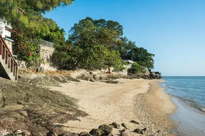 a beach with rocks and trees and the ocean at Lost Paradise Resort in Batu Ferringhi