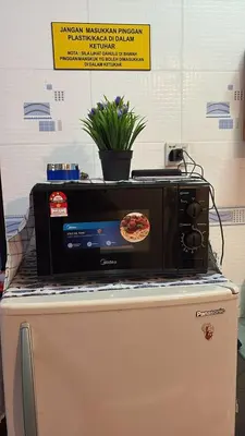 a microwave on top of a refrigerator with a pizza on it at Muslim Apartment Homestay in Tanah Rata