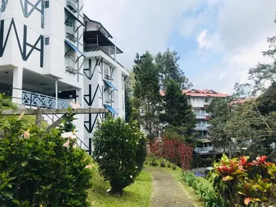 a white apartment building with a garden in front of it at MERLIN HOME DESA ANTHURIUM in Tanah Rata