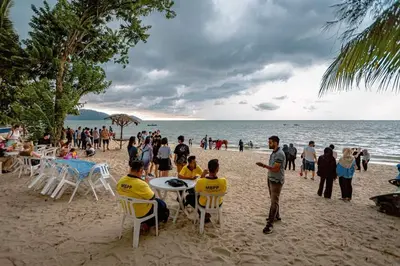 a group of people sitting at tables on the beach at EXECUTIVES Pantai Seaview Batu Ferringhi 2704 - 2 Bedrooms in Batu Ferringhi