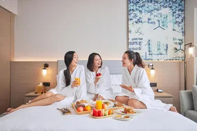 a group of three women sitting on a bed with a tray of food at Courtyard by Marriott Penang in George Town