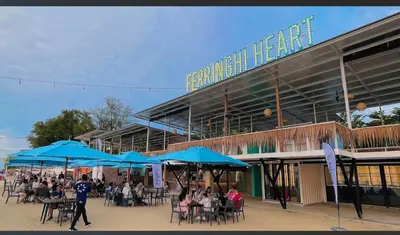 a group of people sitting at tables under blue umbrellas at VIP Seaview Resort Batu Ferringhi 2104 - 2 Rooms in Batu Ferringhi