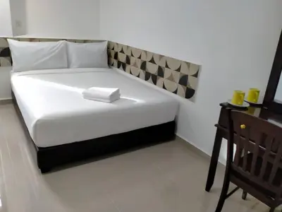 a white bed in a room with a wooden chair at Grand Bagan Hotel in Butterworth