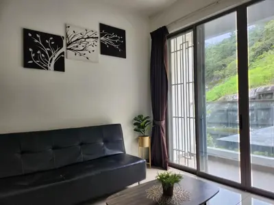 a living room with a black couch and a large window at Relax Bear Homestay in Tanah Rata