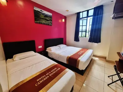 two beds in a room with a red wall at Hotel Sun Birds in Cameron Highlands