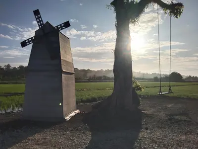 a monument next to a tree with the sun behind it at Casa Villa Homestay Sekinchan in Sekincan