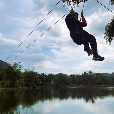 a man is hanging on a rope over a river at Sahom Valley Resort - Agro & Eco Park in Kampar
