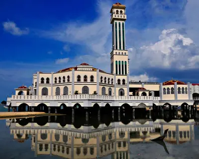 a building with a clock tower with its reflection in the water at EE's Beach House - Homestay 3 min walk to beach in Batu Ferringhi