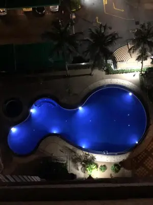 a large blue swimming pool with palm trees at night at Beach Resort Home Stay SRI SAYANG APARTMENT BATU FERRINGHI 2BEDROOM in Batu Ferringhi