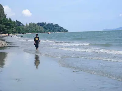 a man walking on the beach near the ocean at KAMILA MOTEL TELUK SENANGIN in Lumut