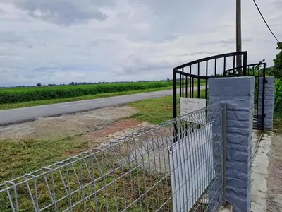a fence next to a road next to a field at Room/Homestay NazaDja in Sungai Besar